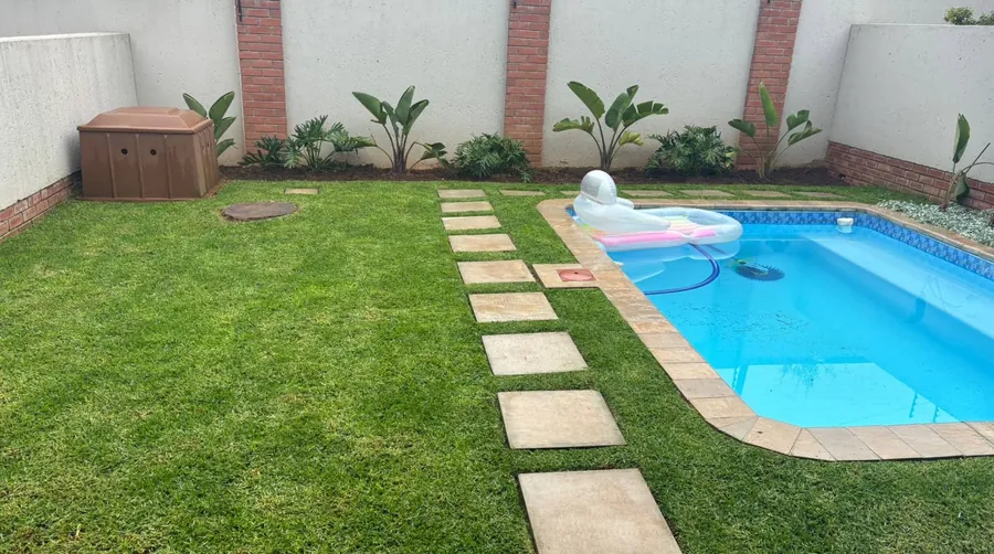 Pool garden with even green lawn, sandstone stepping stones and planted beds along a white wall