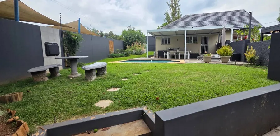 Renovated back garden with lawn, stepping stones, concrete benches and table, and a covered patio by the pool